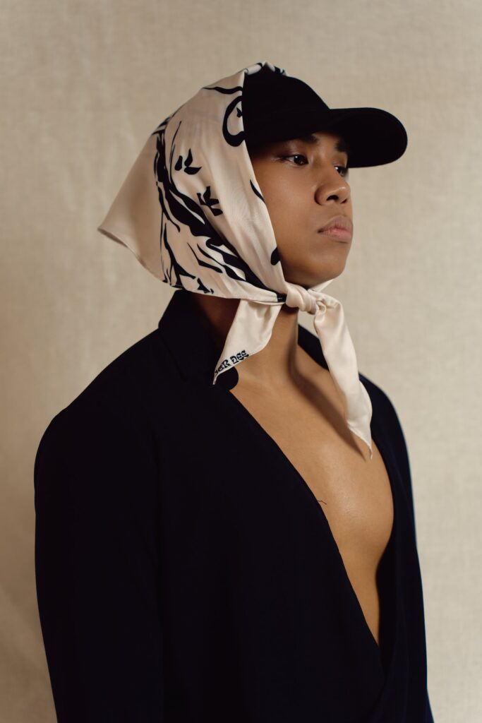 Model wearing the By The Tree cream diamond scarf tied over a black cap