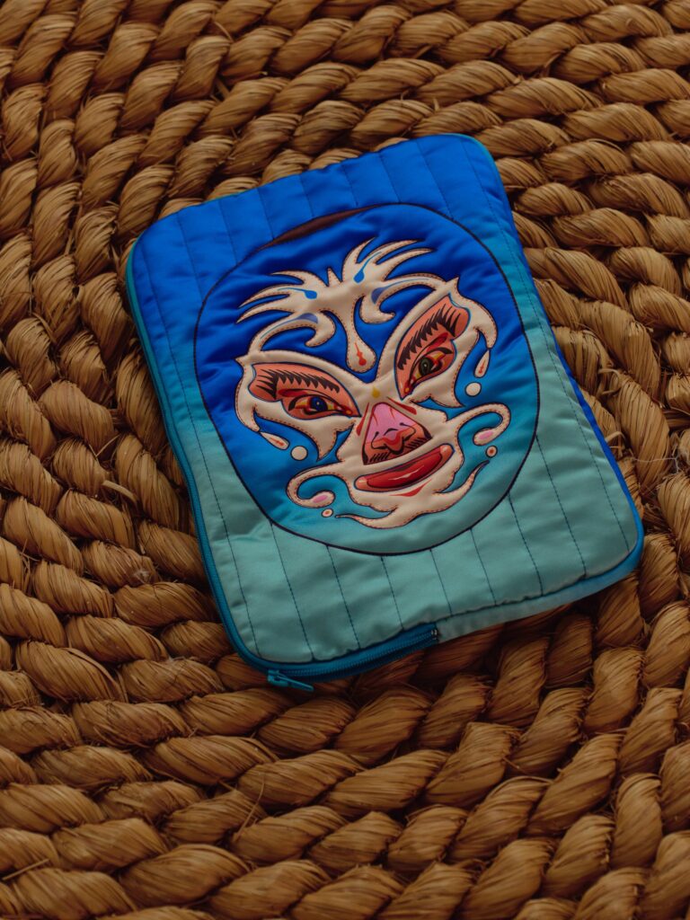 Blue quilted laptop bag with luchador mask artwork on a woven mat