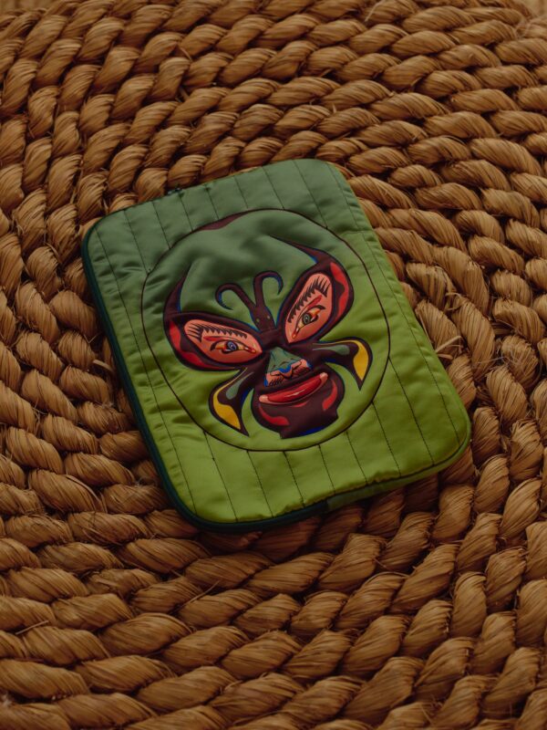 Green quilted laptop bag with luchador mask artwork on a woven mat