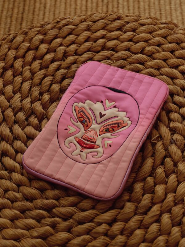 Pink quilted laptop bag with luchador mask artwork on a woven mat