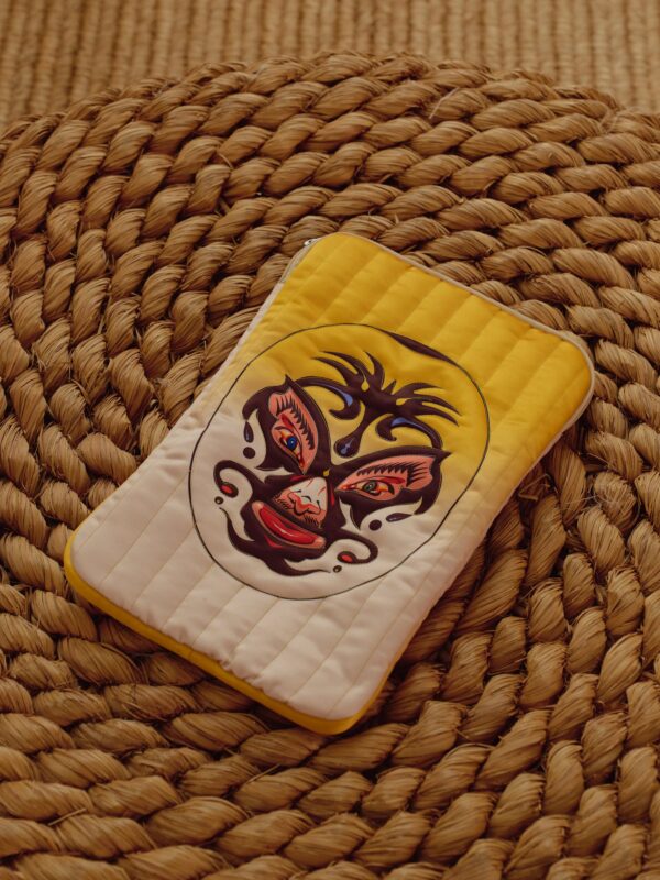Yellow and cream quilted laptop bag with luchador mask artwork on a woven mat