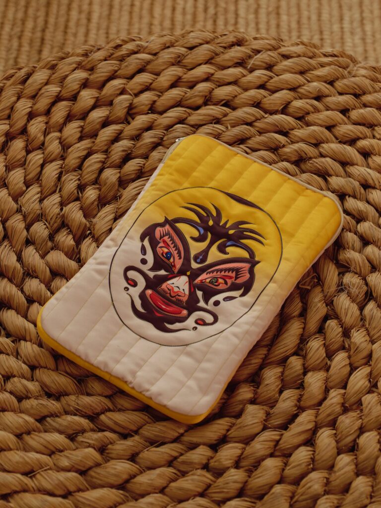 Yellow and cream quilted laptop bag with luchador mask artwork on a woven mat