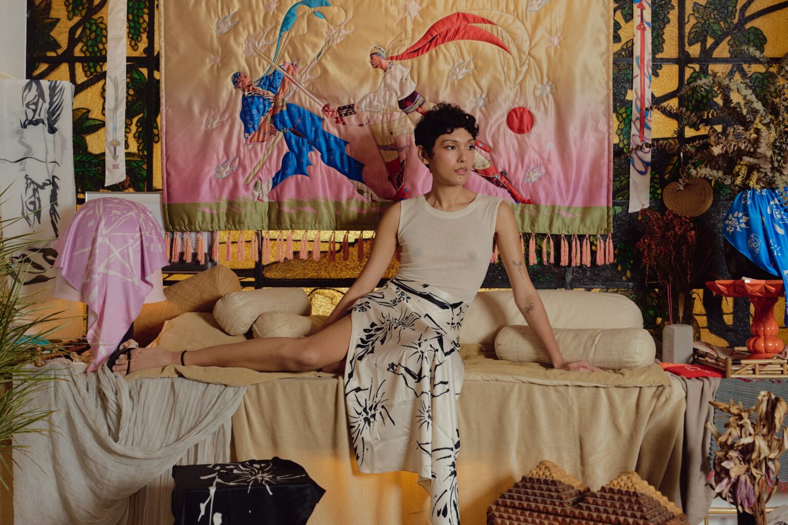 Model reclining in a room of Jer Dee textiles beneath the Swordfight Tapestry